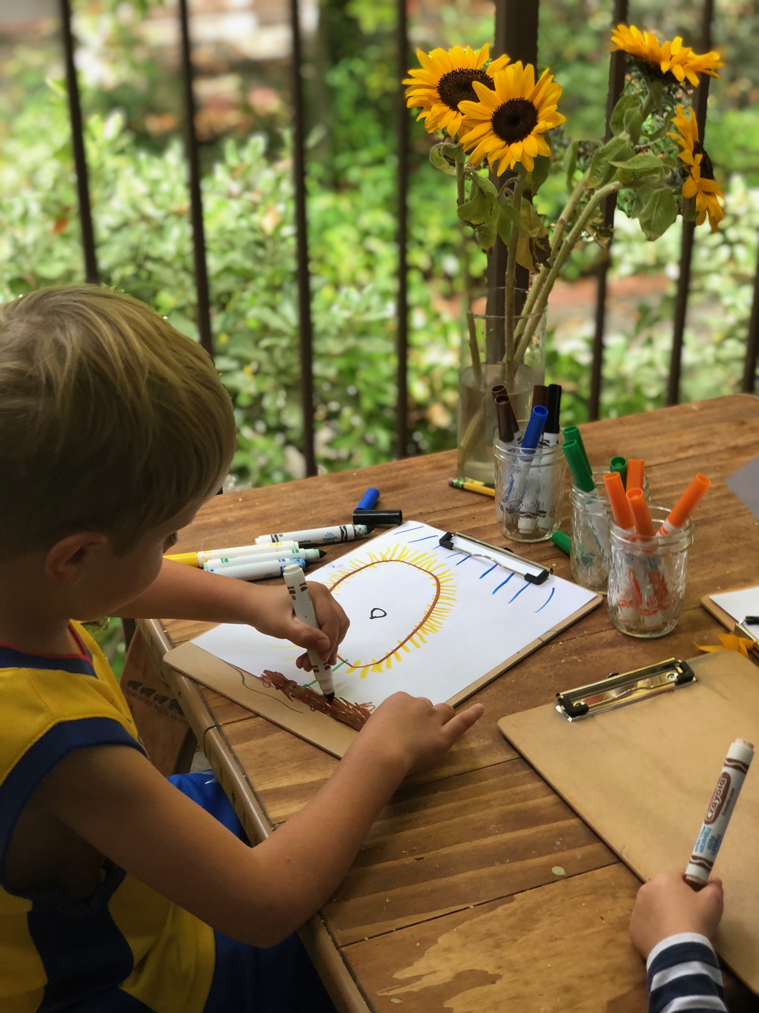 Child drawing outdoors surrounded by sunflowers at The Ross Preschool