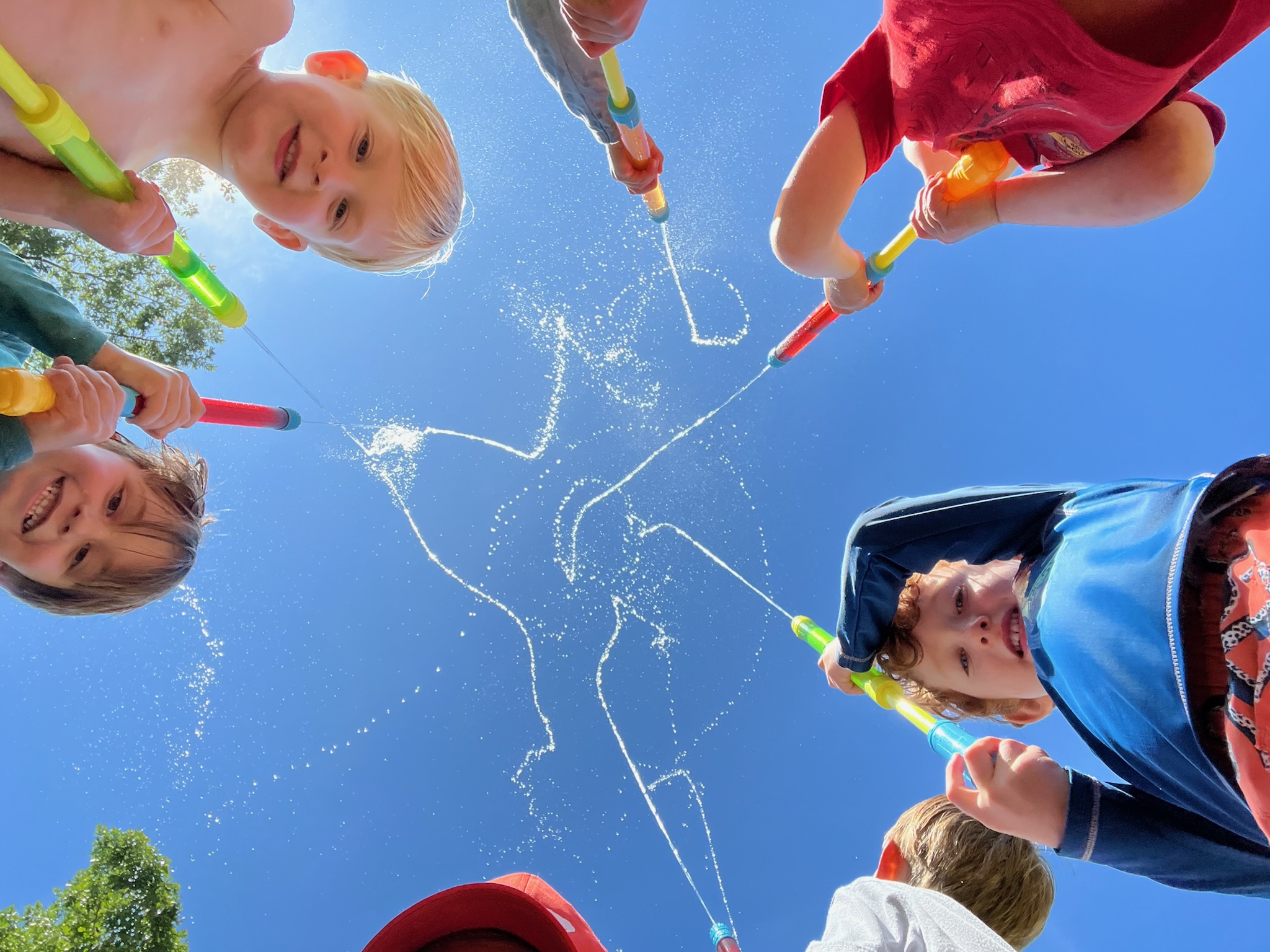 Children shooting water squirters up into the blue sky